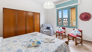 Une chambre à coucher avec un lit, une armoire, une fenêtre donnant sur un beau paysage et une chaise avec un coussin.