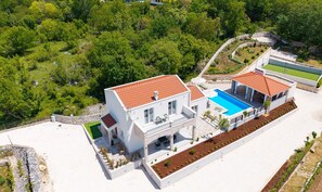 Een modern huis met twee verdiepingen, met een zwembad, omringd door weelderige begroeiing en een stenen keerwand.