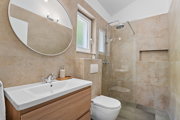 A bathroom with a large round mirror, a sink, a toilet, and a shower area.