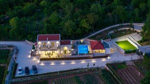 A two-story house with a swimming pool, a tennis court, and a landscaped garden.