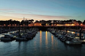 A marina at dusk with boats docked and buildings in the background.