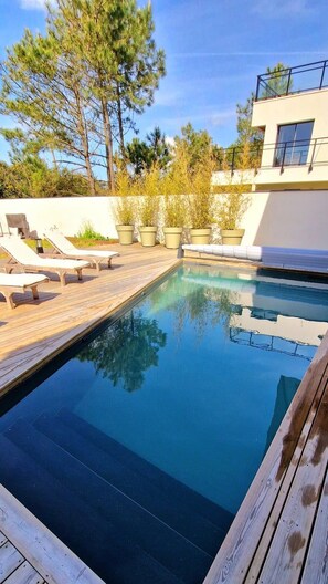 A swimming pool with a wooden deck, lounge chairs, and potted plants.
