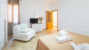A hotel room with a bed, a TV, a desk, and a door leading to another room. - Apartment 'Libellula' with Balcony, Wi-Fi and Air Conditioning (Siracusa)