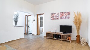 A spacious living area with a wooden floor, a TV on a wooden stand, and two floral paintings on the wall. - Apartment 'Libellula' with Balcony, Wi-Fi and Air Conditioning (Siracusa)