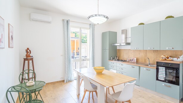 A modern kitchen with a wooden table, white chairs, and a green metal chair. - Apartment 'Libellula' with Balcony, Wi-Fi and Air Conditioning (Siracusa)