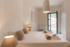 Quarto com cama, luminária, ar condicionado fixado na parede e vista através de uma porta.