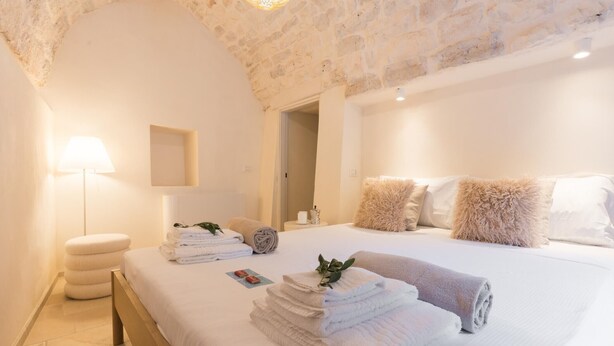 A bedroom with a stone ceiling, a bed with white linens, a bedside table with a lamp, and a door leading to another room. - Palazzina Tommaso Sea View & Wellness "Adults Only" between Ostuni and Fasano (Fasano)