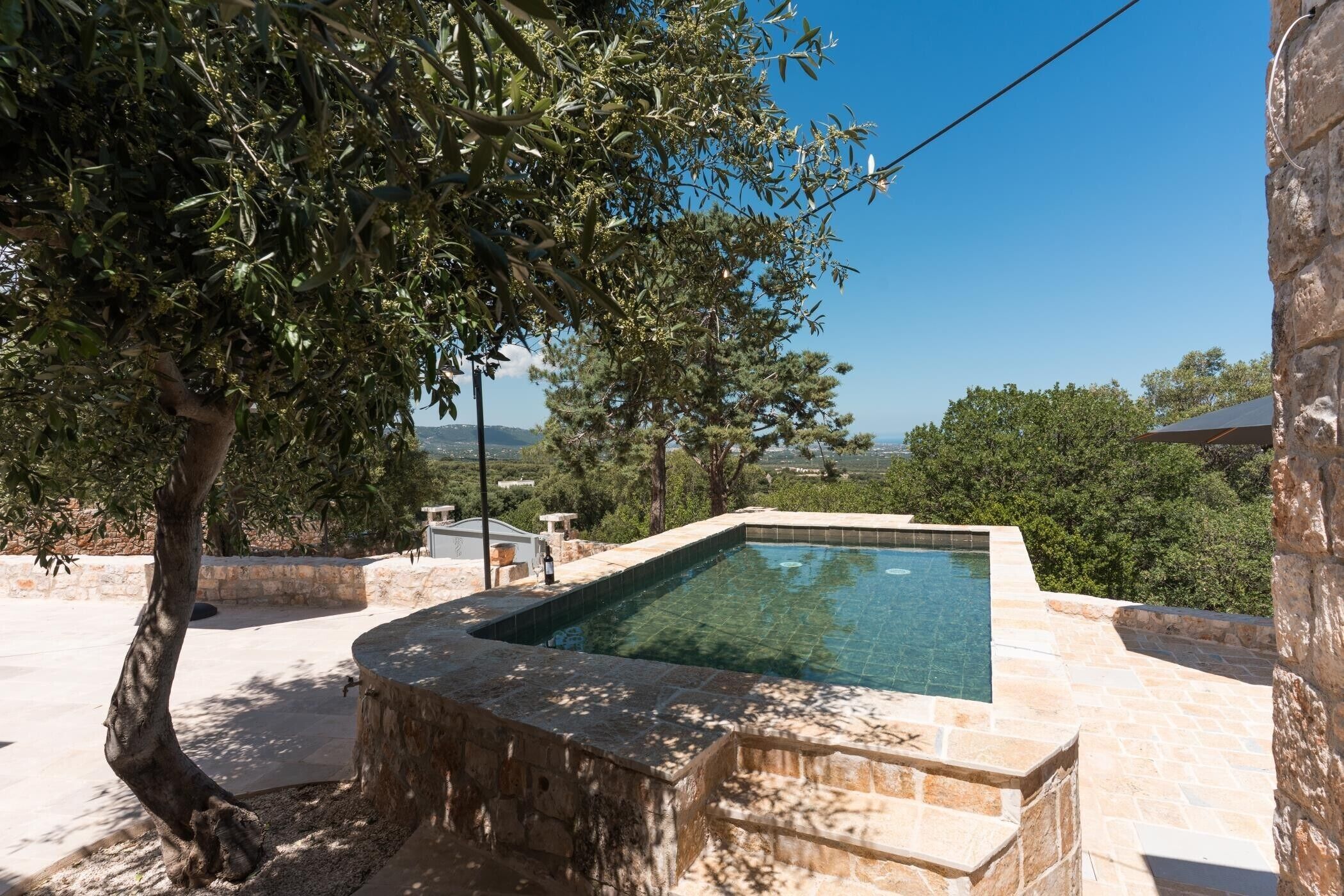 Piscina con pareti in pietra, un albero e vista sul paesaggio.