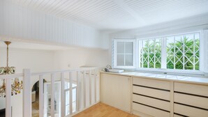 Une pièce avec un plafond blanc, une fenêtre donnant sur un paysage verdoyant, une rambarde blanche et un plancher en bois.