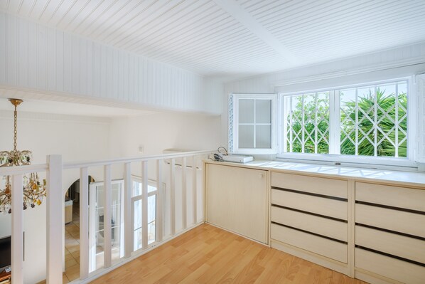 Una habitación con techo blanco, ventana con vistas a zonas verdes, barandilla blanca y suelo de madera.