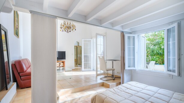Une chambre à coucher avec un lit, un fauteuil rouge, un téléviseur et une vue sur l’extérieur par une fenêtre.