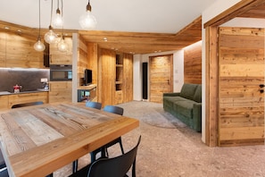 A modern interior with a wooden dining table, chairs, a sofa, and a TV.