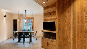 A modern interior with a wooden wall, a TV, a fireplace, and a dining area with chairs and a table. - Apartment 'Rododendro' with Mountain View, Private Garden and Wi-Fi (Isolaccia)