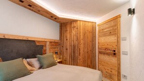 A bedroom with a bed, wooden panel walls, a nightstand, and a lamp. - Apartment 'Rododendro' with Mountain View, Private Garden and Wi-Fi (Isolaccia)