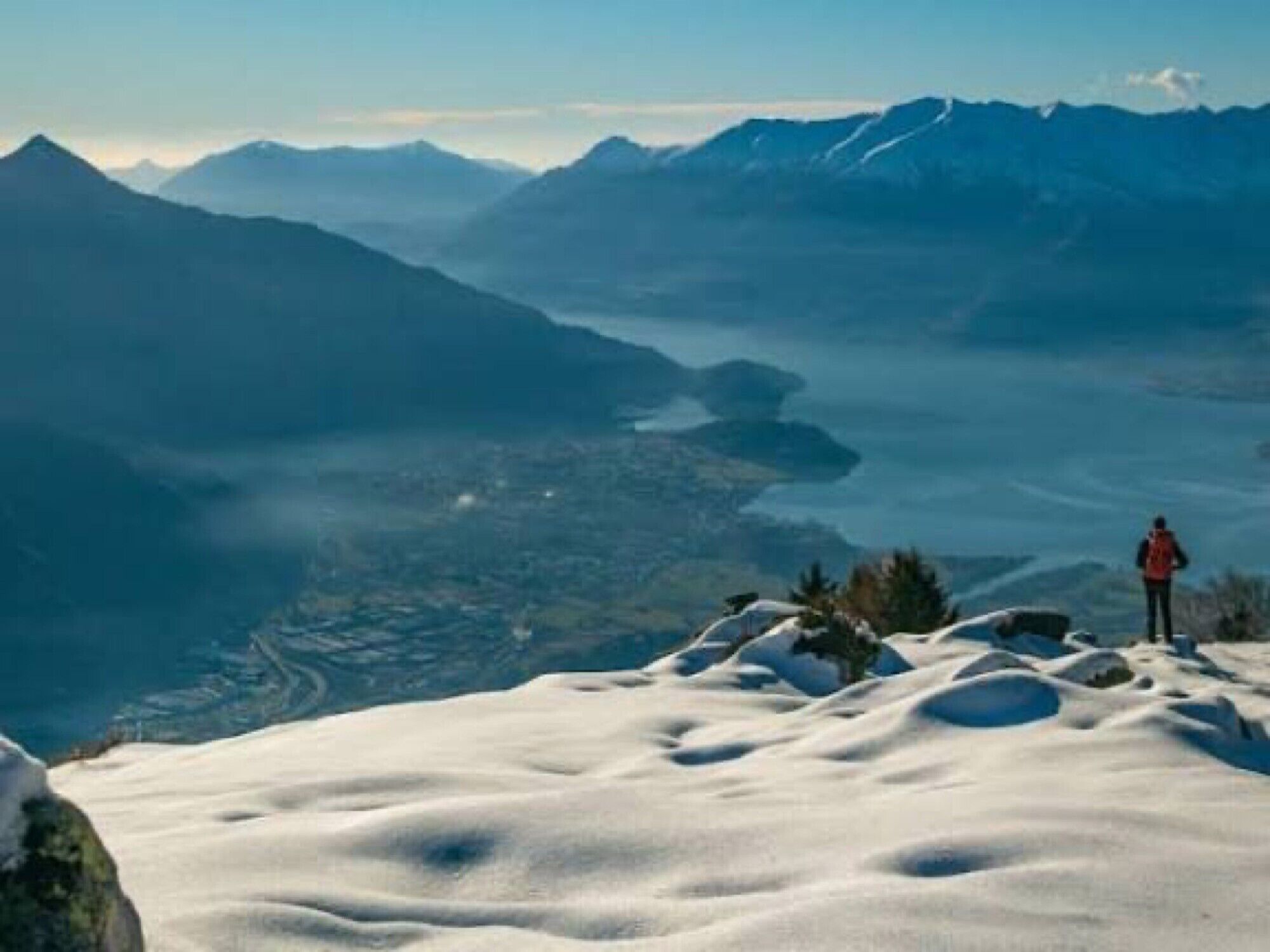Une personne se tient au sommet d’une montagne enneigée, d’où l’on peut admirer des montagnes et des vallées lointaines.