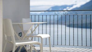 A balcony with a white metal table and chair, overlooking a body of water with mountains in the background. - Holiday Home 'Il Nido Del Colibrì' with Lake View, Private Terrace & Wi-Fi (Stazzona)