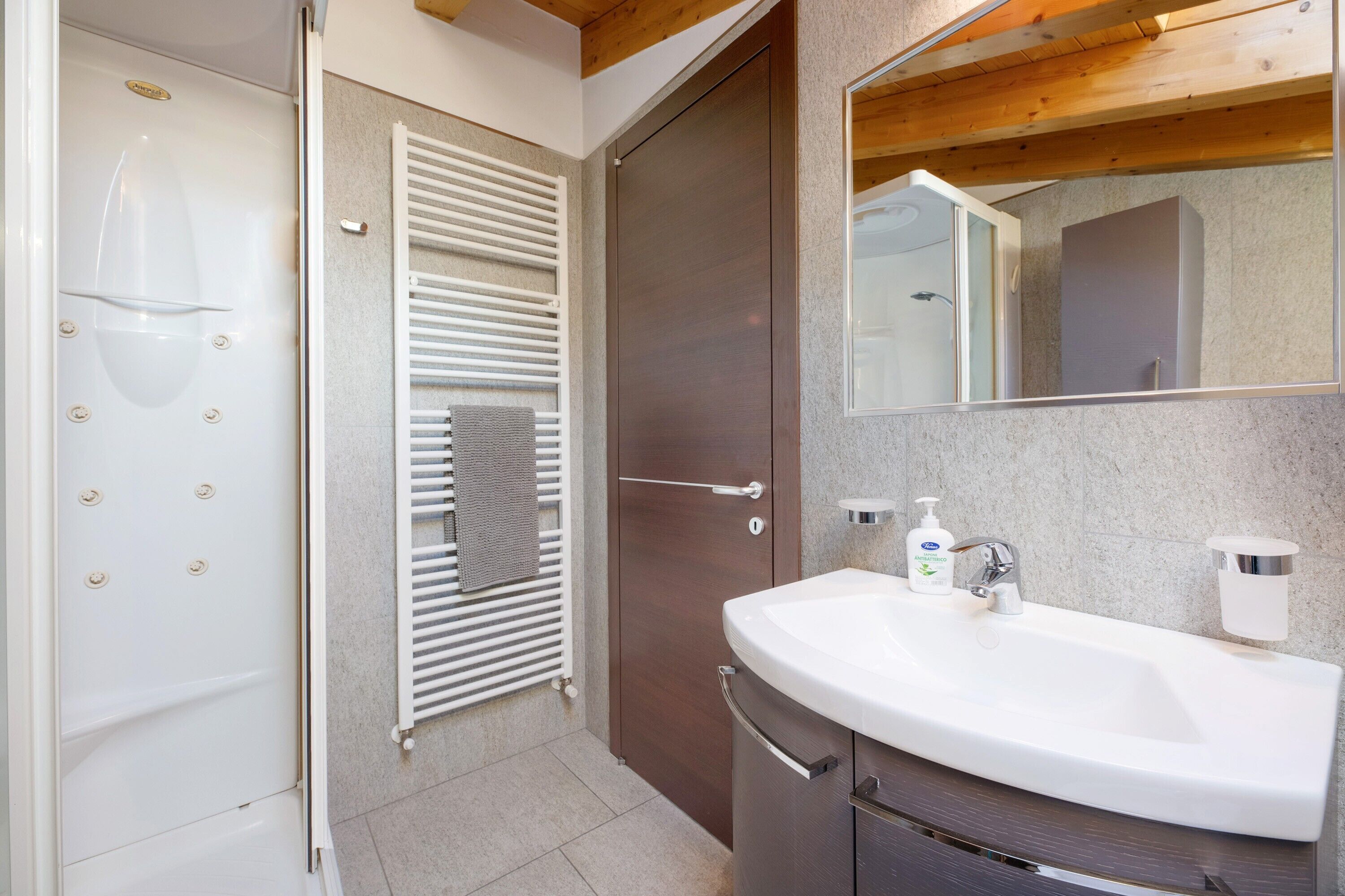 Une salle de bain avec un lavabo blanc, un miroir, un porte-serviettes et une porte de douche.