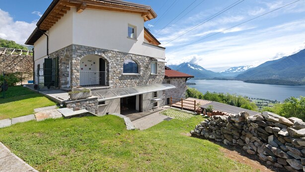 A two-story house with stone facade, a balcony, and a view of a lake and mountains. - Holiday Home 'Il Nido Del Colibrì' with Lake View, Private Terrace & Wi-Fi (Stazzona)