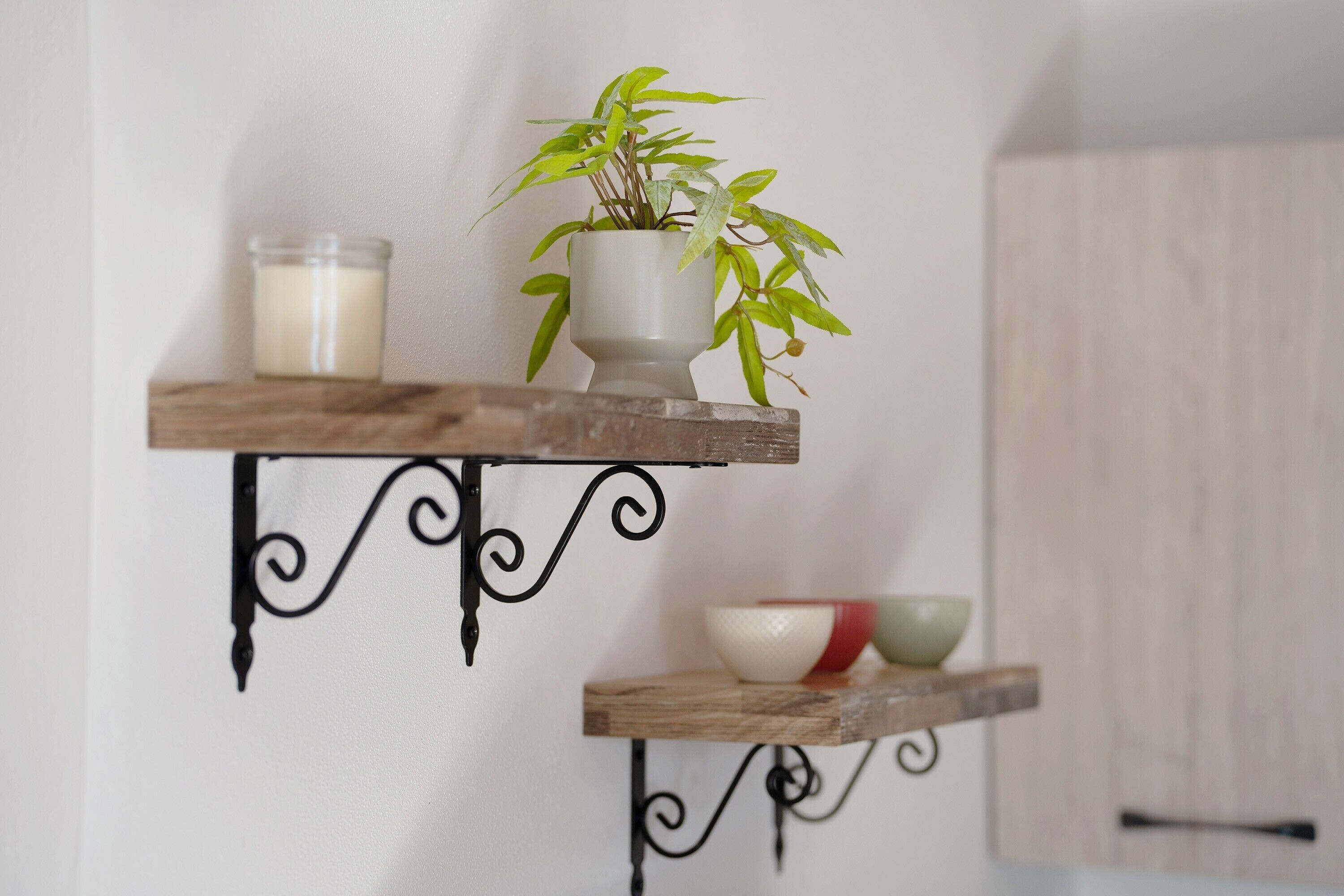 Deux étagères en bois, dotées de supports en métal noir, sur lesquelles sont posées une plante en pot et une bougie.
