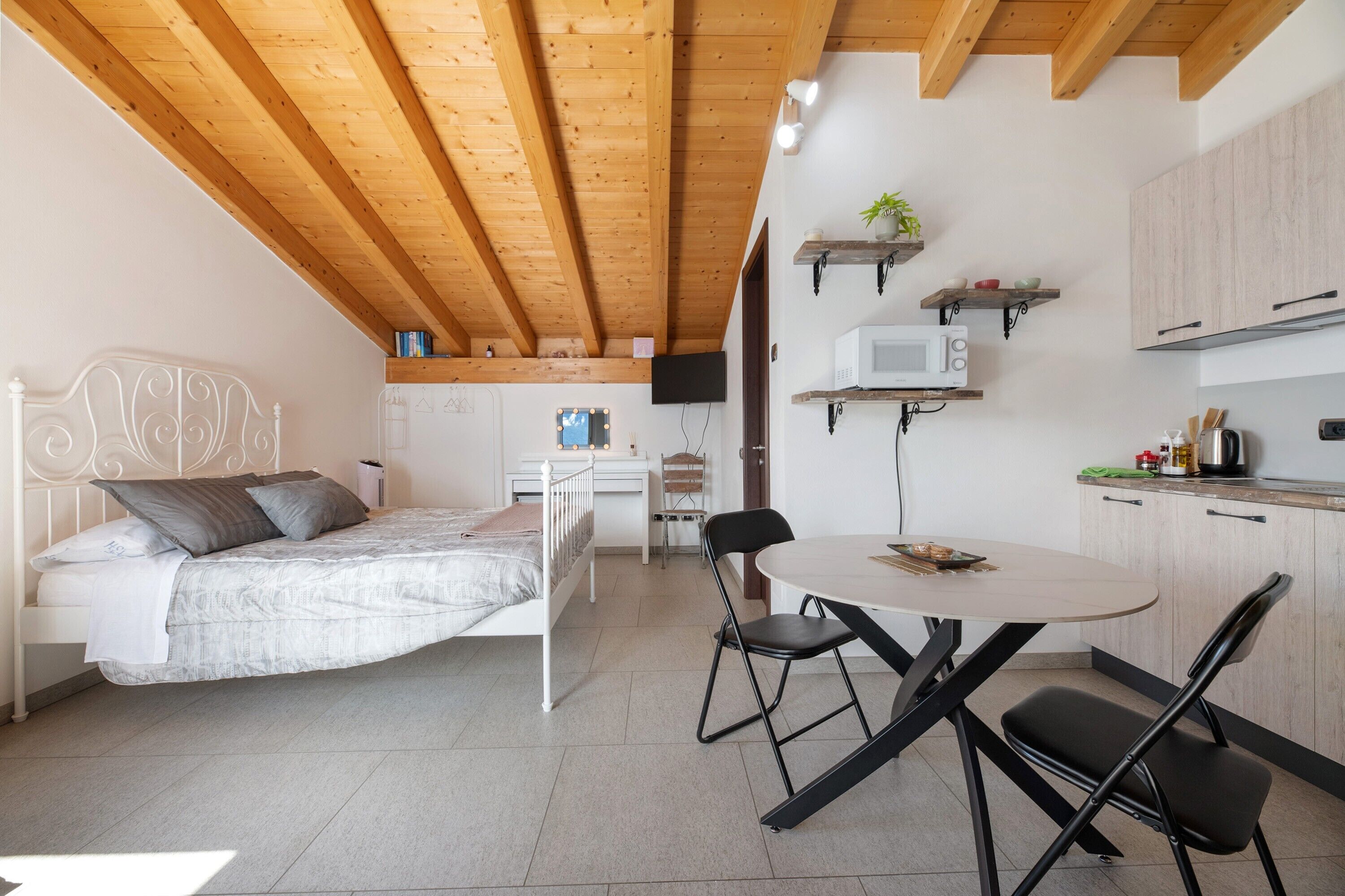 Een slaapkamer met een bed, een bureau, een stoel en een kitchenette met een magnetron en kastjes.