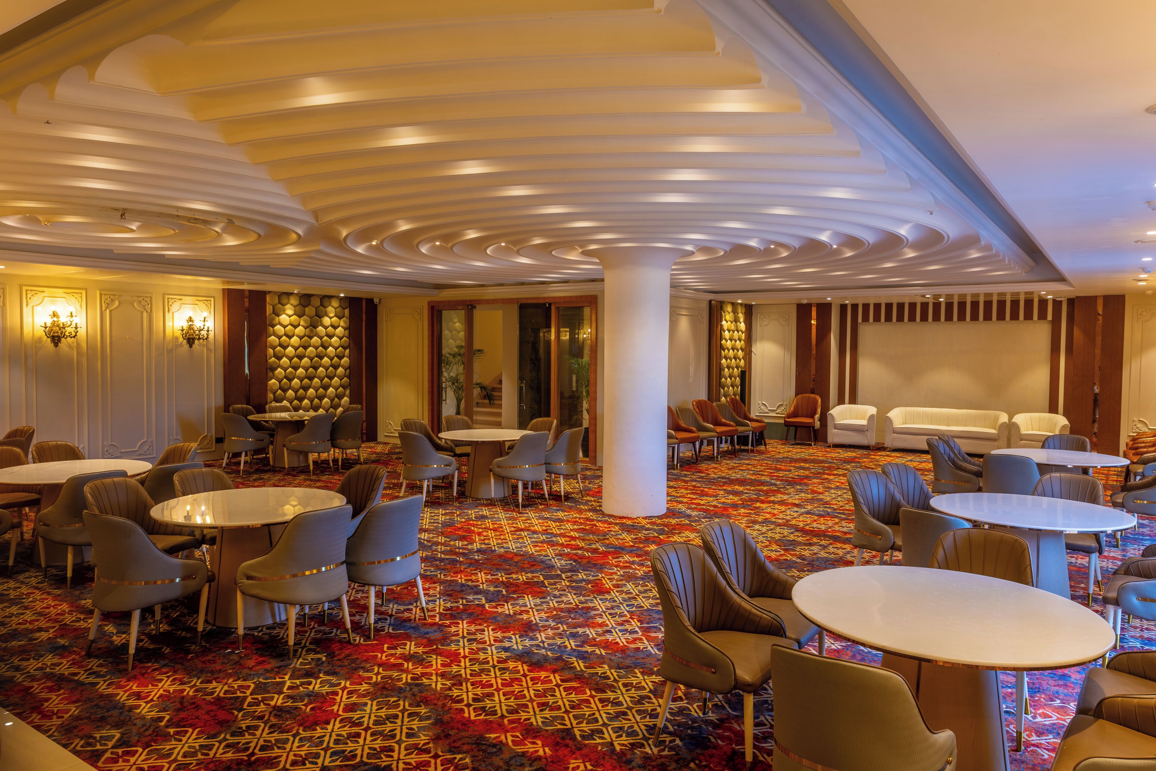 A hotel lobby with round tables, chairs, a patterned carpet, and a decorative ceiling.