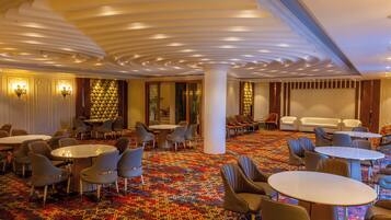 A hotel lobby with round tables, chairs, a patterned carpet, and a decorative ceiling.