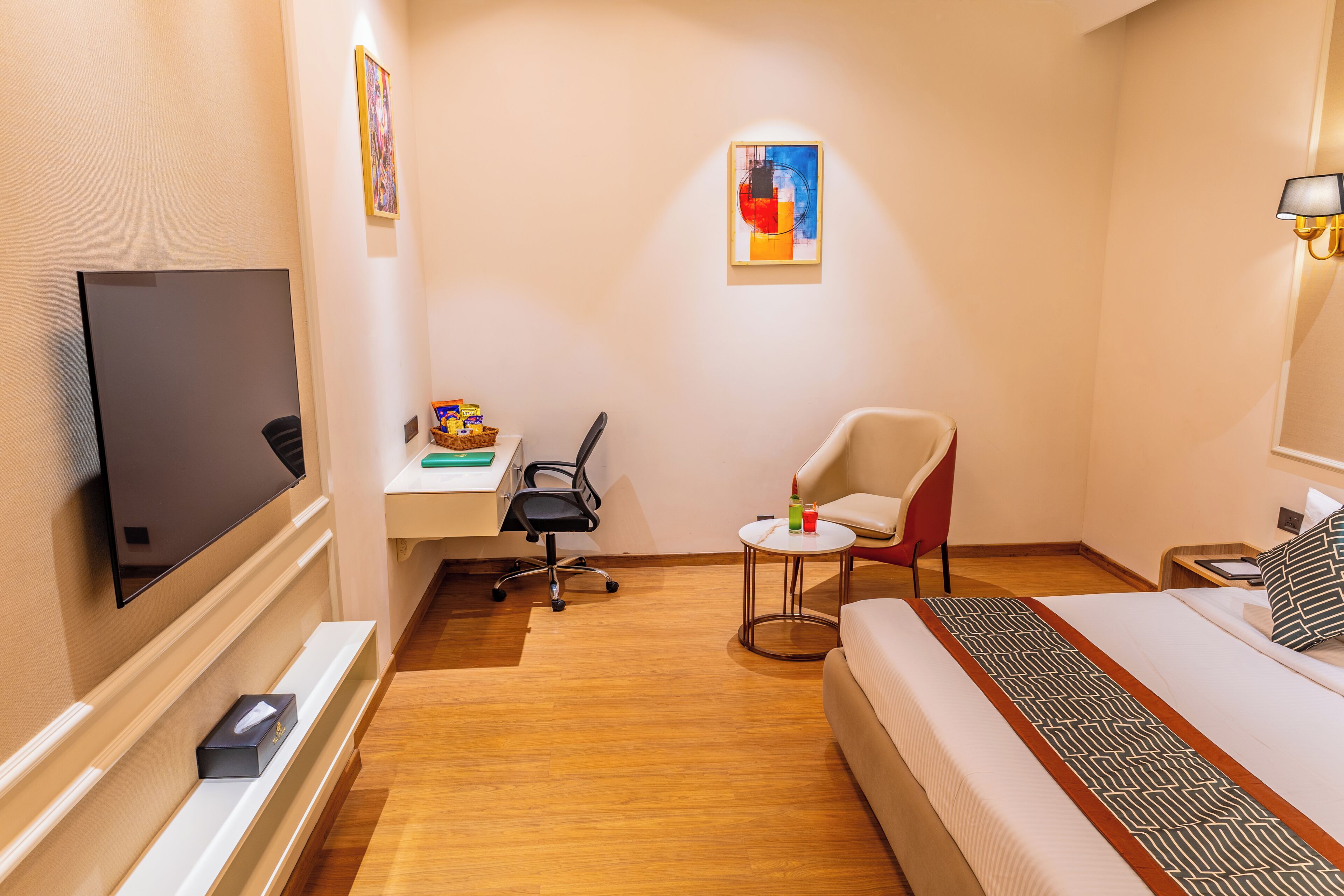 Hotellihuone, jossa on sänky, työpöytä, tuoli, televisio ja pieni pöytä.