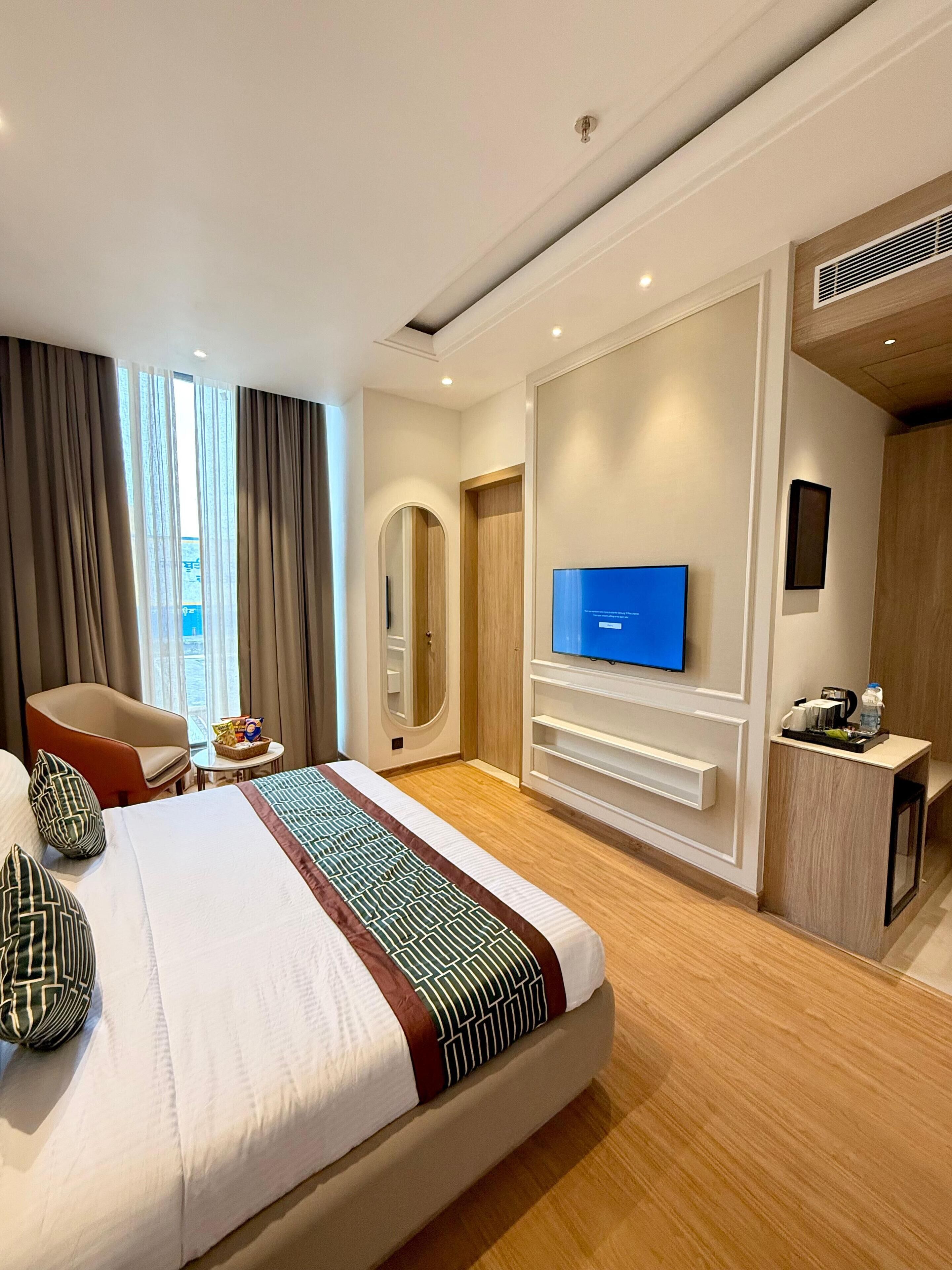 A hotel room with a large bed, a television, a desk with a chair, and a window with curtains.