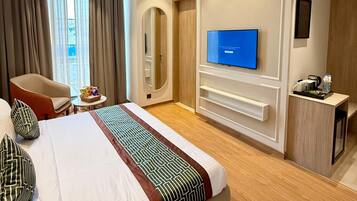 A hotel room with a large bed, a television, a desk with a chair, and a window with curtains.