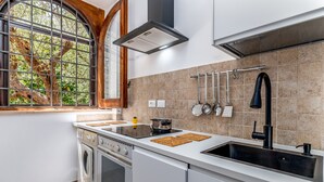 Una cocina moderna con horno empotrado, estufa, pileta y ventana con vista a árboles.