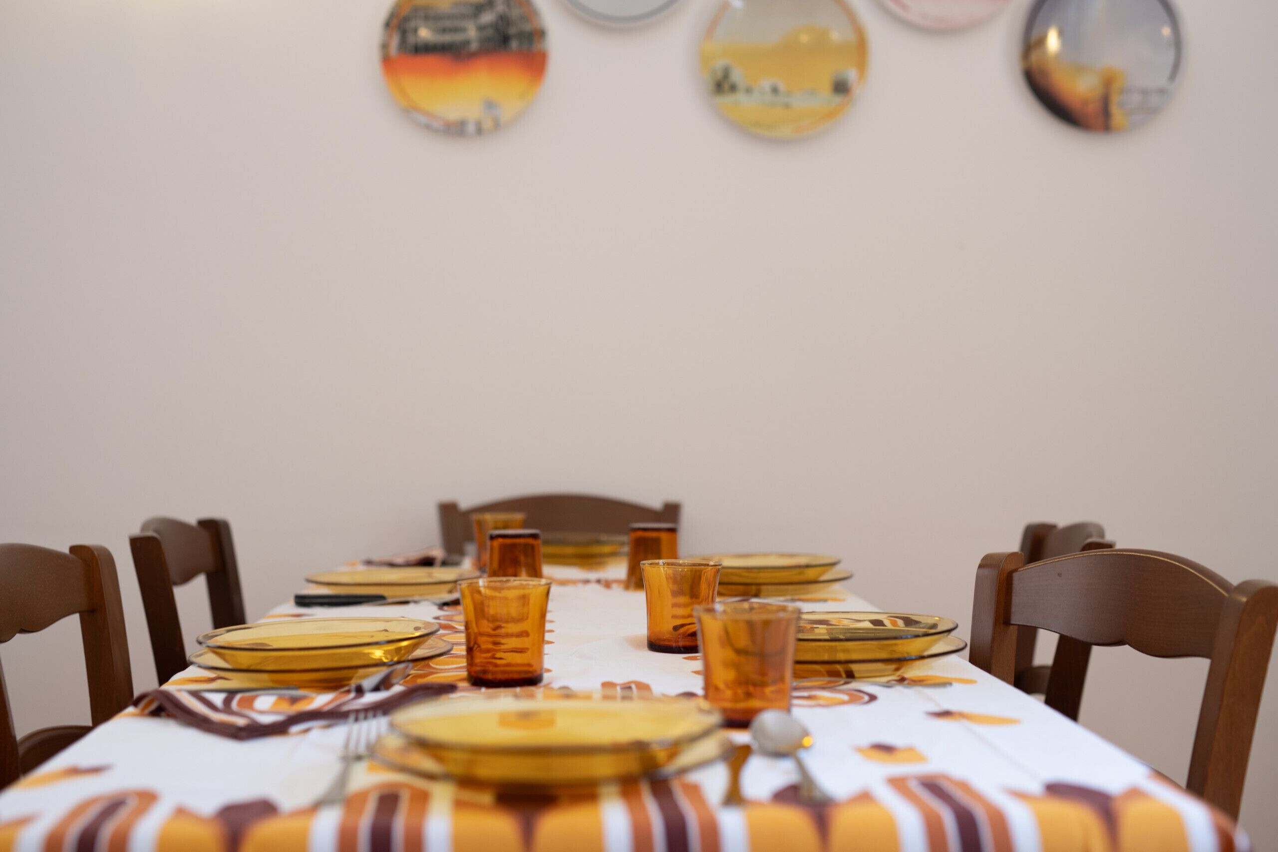 Una mesa de comedor dispuesta con vasos y platos, rodeada de sillas de madera.