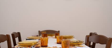 Una mesa de comedor dispuesta con vasos y platos, rodeada de sillas de madera.