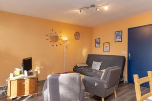 Une pièce comprenant un canapé, un bureau avec un ordinateur, une lampe, une horloge et une porte.