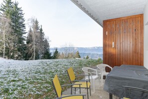 Une pièce comprenant un lit, deux chaises, une table et donnant sur un paysage enneigé, avec des arbres et du sol recouverts de neige.