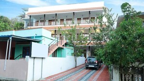 A two-story building with a balcony on the upper floor, a covered walkway, and a parked car. - Periyar Canopy Thekkady (Kumily)
