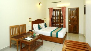 A hotel room with a bed, wooden furniture, a desk, and a door. - Periyar Canopy Thekkady (Kumily)