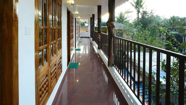 A corridor with wooden doors, a balcony with a railing, and a view of greenery outside. - Periyar Canopy Thekkady (Kumily)