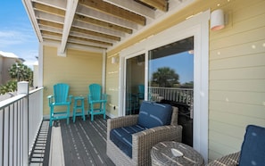 A balcony with wicker furniture, a sliding glass door, and a view of palm trees.