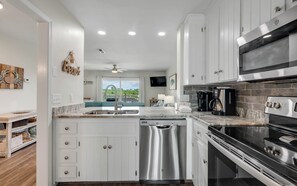 A modern kitchen with white cabinets, stainless steel appliances, and a large island with a dishwasher. - Inlet Beach + Gulf View, Pet Friendly & Bikes (Inlet Beach)