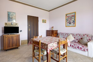 A dining area with a table, chairs, a television on a cabinet, a sofa, and a poster on the wall. - Apartment 'Carbone' with Private Terrace, Wi-Fi and Air Conditioning (Roddi)