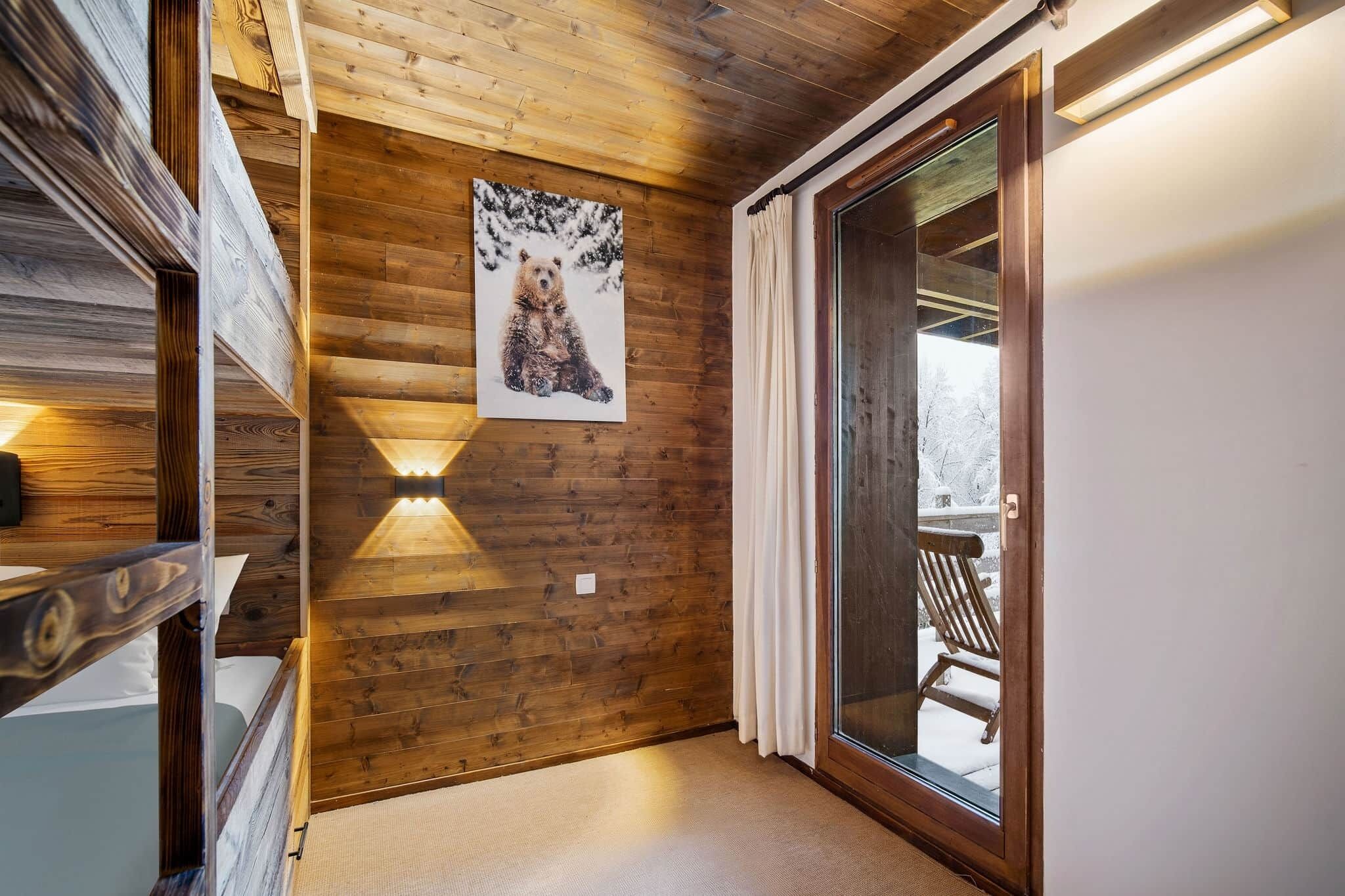 A wooden interior with a bear painting, a sliding glass door to a snowy outdoor area, and a wooden bench.