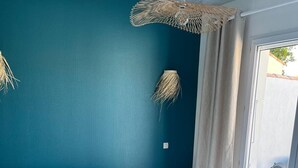 Une chambre à coucher avec un lit, un mur bleu, un luminaire suspendu et une fenêtre avec des rideaux.
