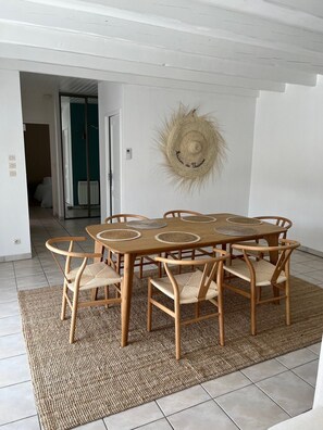 Een eetgedeelte met een houten tafel en stoelen, een geweven vloerkleed en een strooien hoed aan de muur.