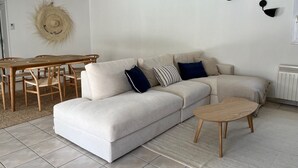 Un salon comprenant un canapé, une table basse, une table à manger avec des chaises et une lampe fixée au mur.