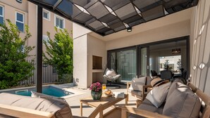 Ein sonniger Sitzbereich im Freien mit Pool, gepolsterten Stühlen und einem Tisch mit Blumenvase.