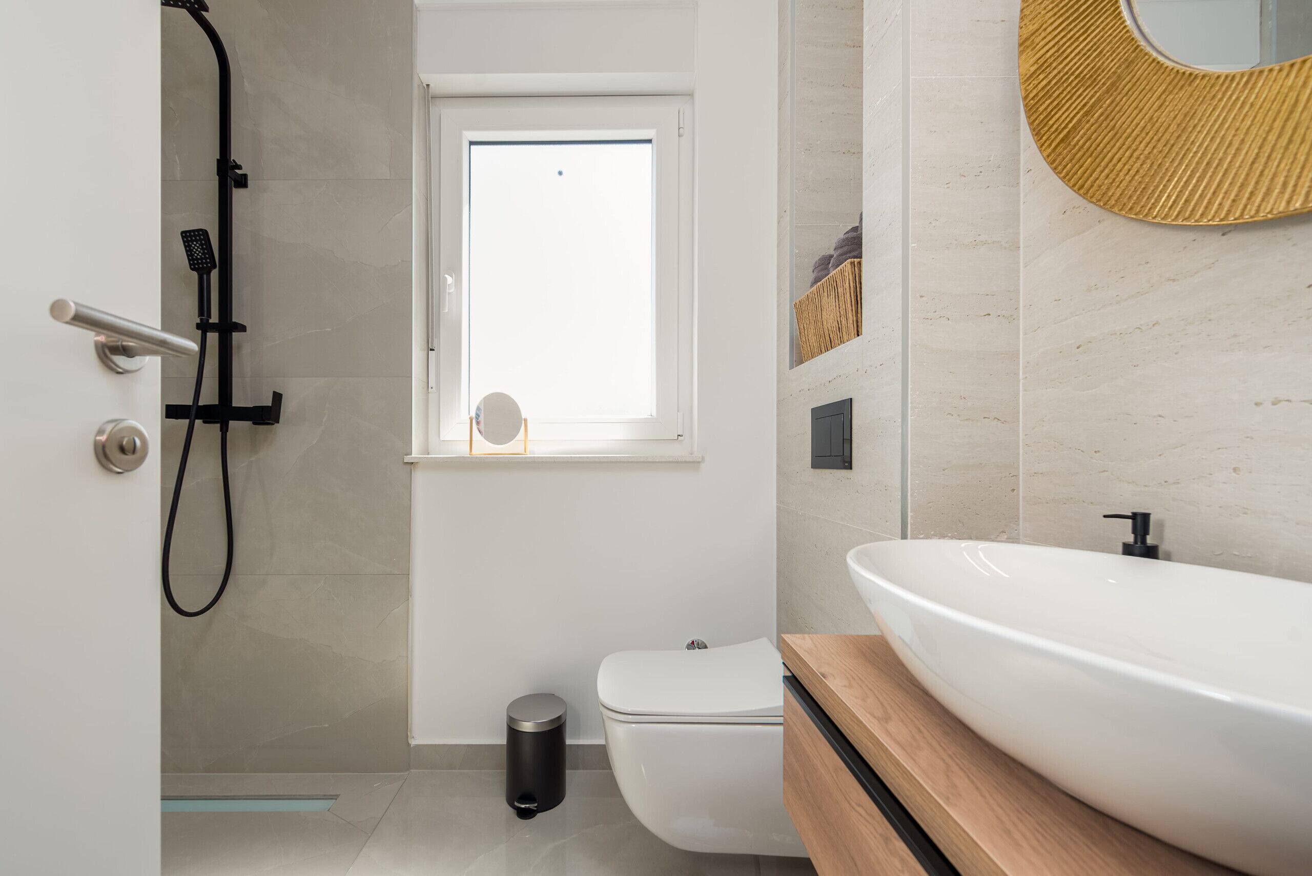 Une salle de bain moderne avec un lavabo blanc, des toilettes, une douche et une fenêtre.
