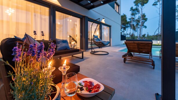 A modern outdoor seating area with a table set for two, featuring a candle, flowers, and a plate of food. - Villa Cvita Zadar Villas (Privlaka)