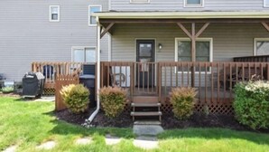 A two-story house with a covered porch, a front door, and a small front yard with a lawn and shrubs.