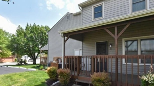 A two-story house with a covered porch, a front door, and a small front yard with landscaping.