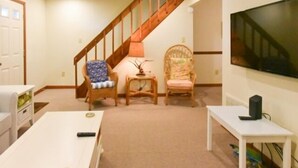 A living room with a white sofa, a small table, a TV, and a staircase.